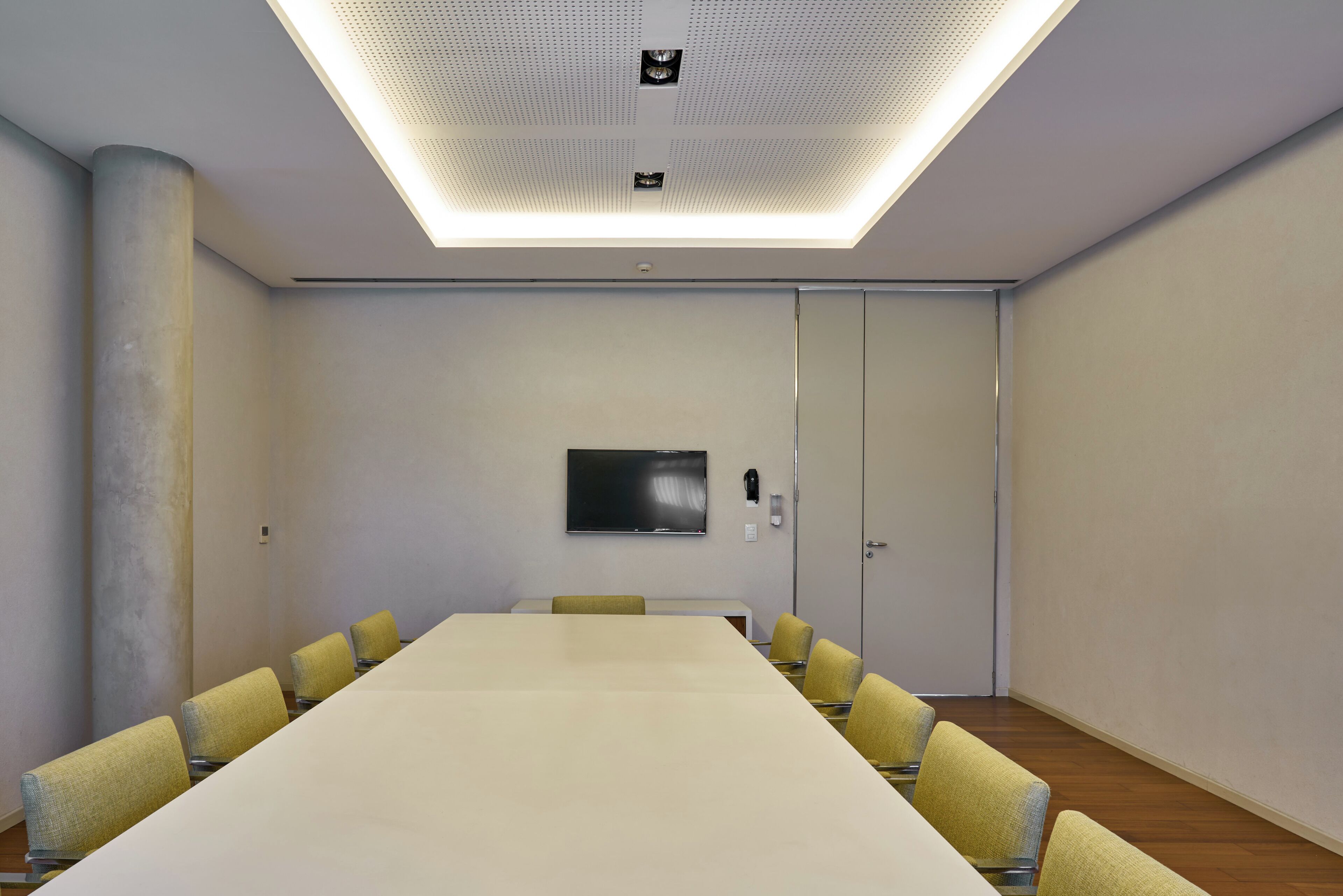 A conference room with a long table, yellow chairs, a flat-screen TV, and a ceiling light fixture.