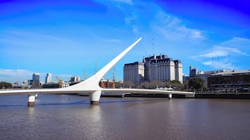 Uma ponte moderna com design branco semelhante a um veleiro, atravessando um rio, com um horizonte urbano ao fundo.