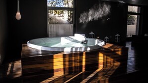 Moderni spa-huone, jossa on poreallas, puulattia ja suuret ikkunat, joista pääsee sisään runsaasti luonnonvaloa.