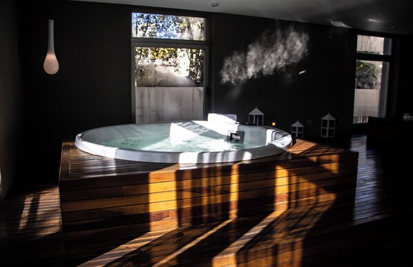 Une salle de spa moderne dotée d’un jacuzzi, de revêtements de sol en bois et de grandes fenêtres laissant entrer la lumière naturelle.