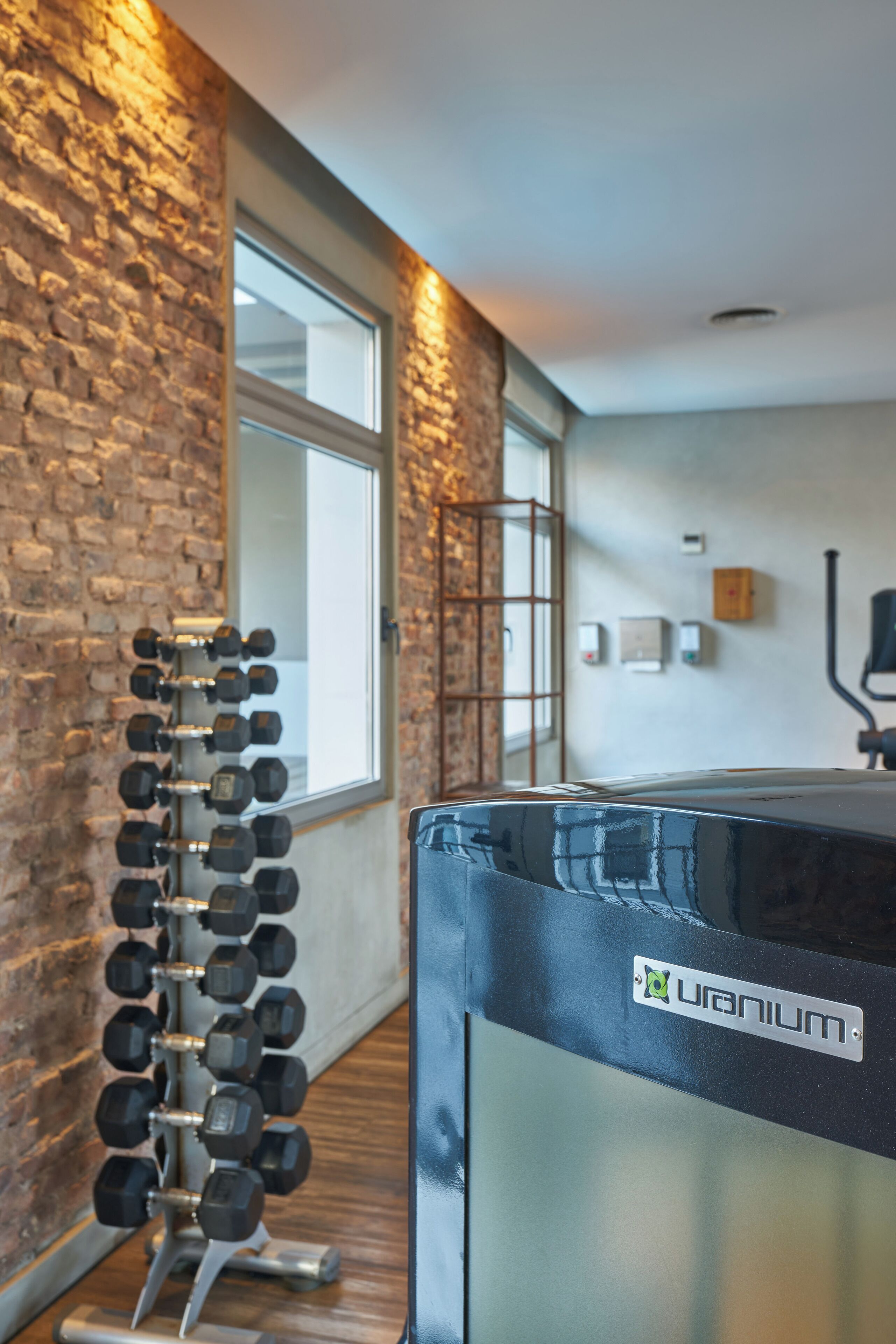 Un gimnasio con pared de piedra, un soporte para mancuernas y una sauna con el rótulo 'Quantum'.