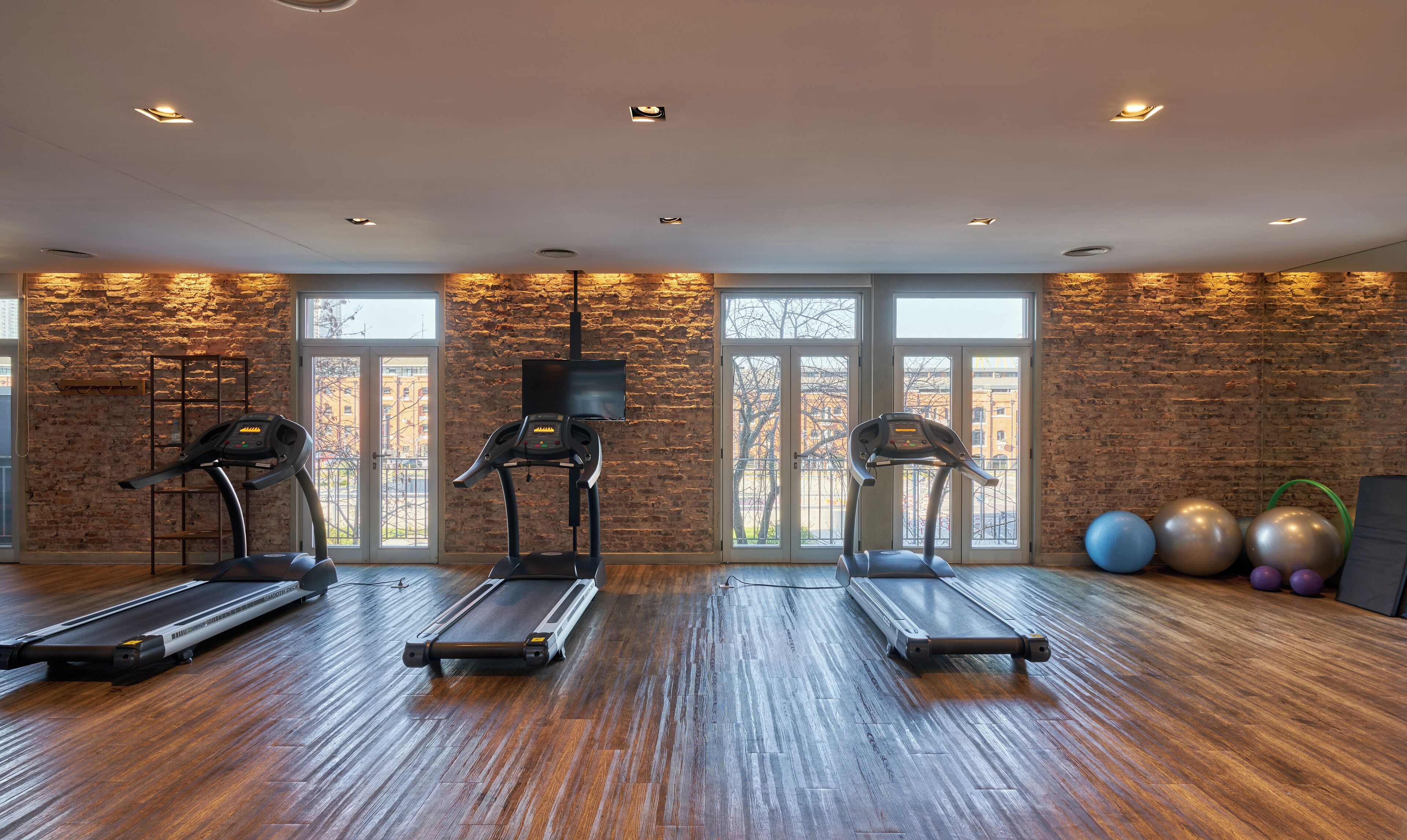 A gym with three treadmills, exercise balls, and a brick wall.