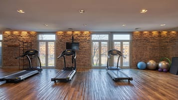 A gym with three treadmills, exercise balls, and a brick wall.