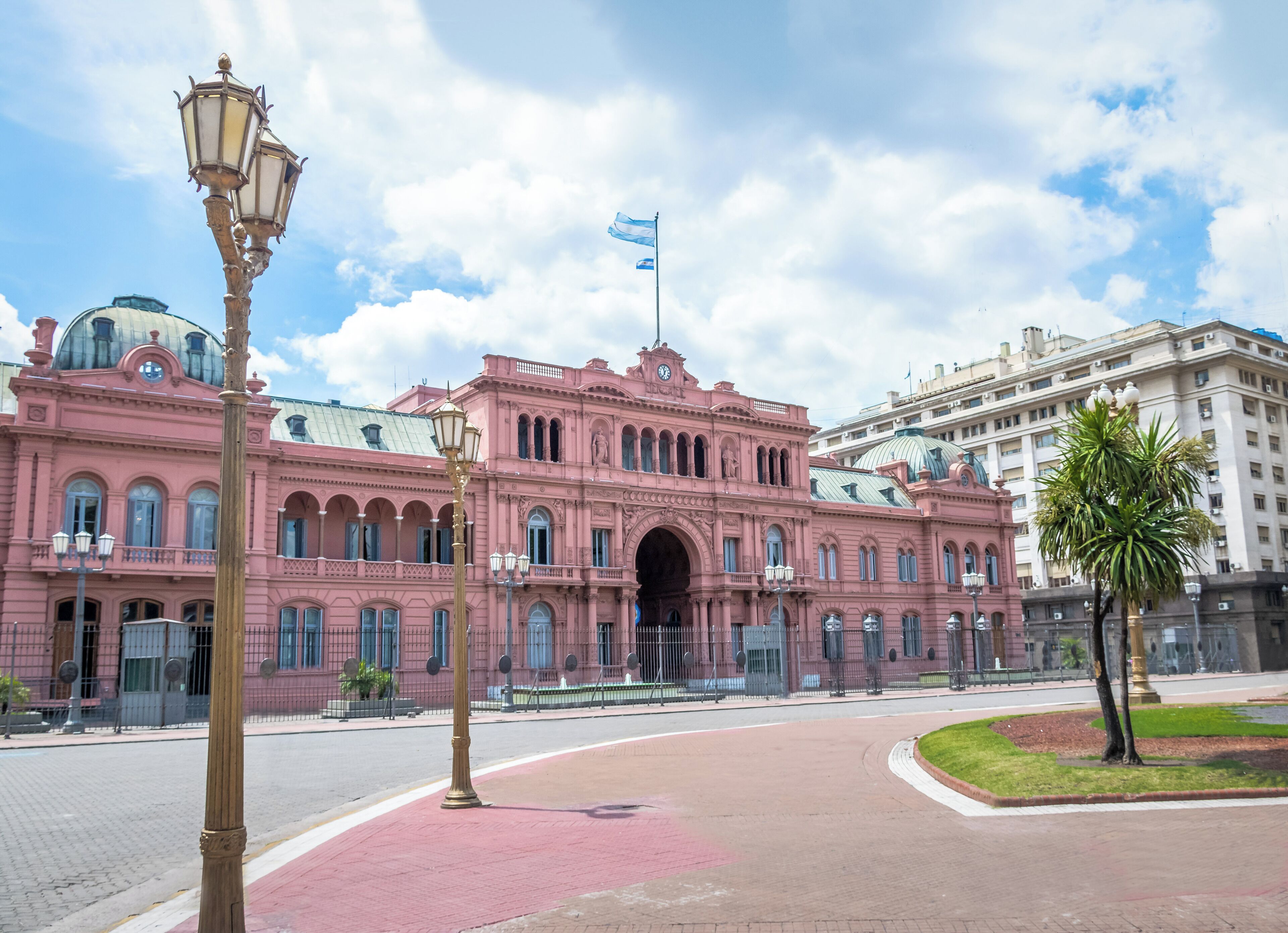 Un edificio histórico rosa con un arco central, una bandera y un farol en primer plano.