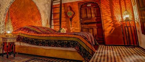 A traditional Moroccan room with a bed, ornate wall decorations, and a patterned floor.