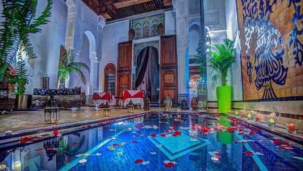 Een luxueus binnenzwembad met betegelde vloer, omringd door decoratieve architectuur en potplanten.