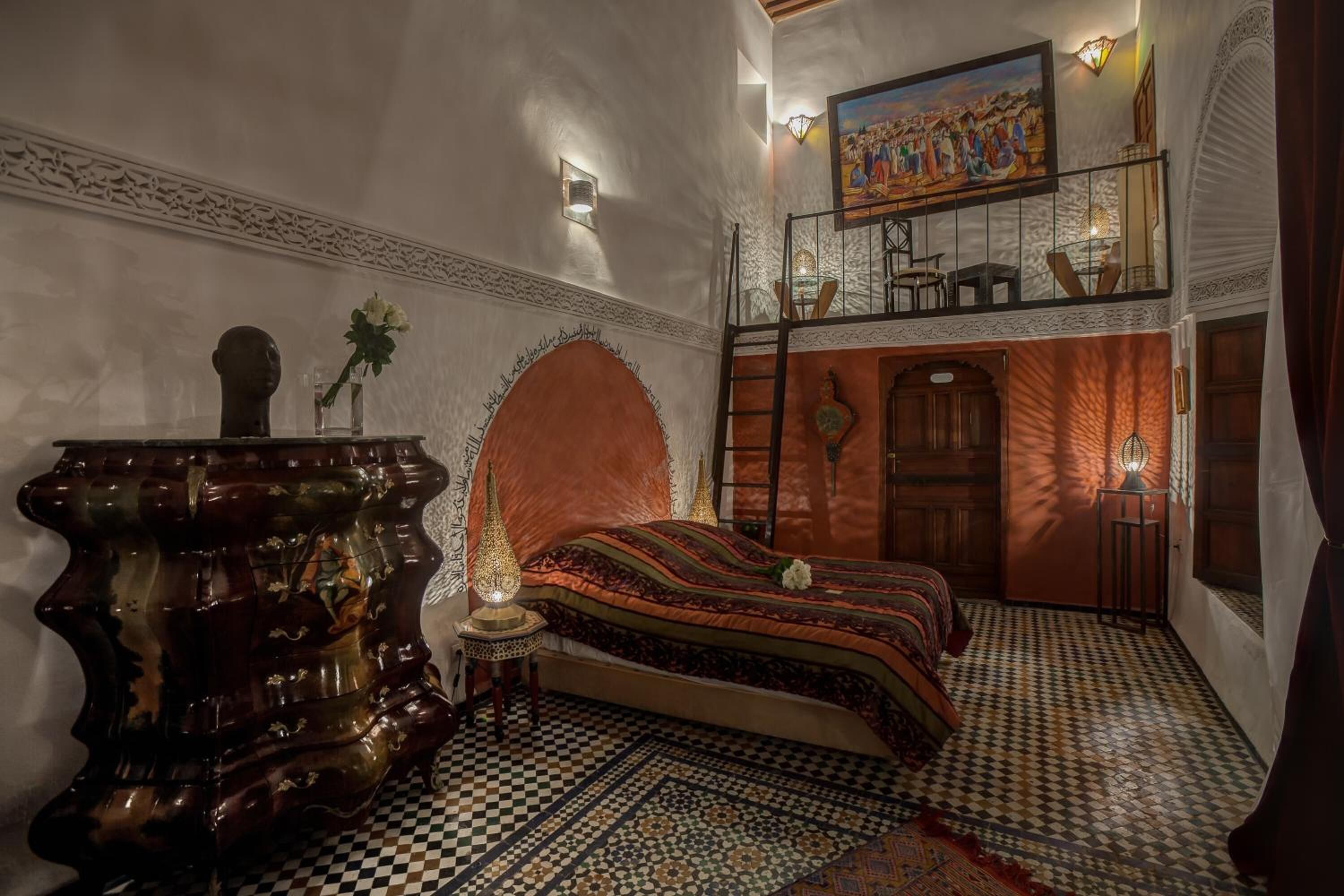 Un dormitorio con suelo a cuadros, una cama con colcha estampada, un aparador de madera, una mesita de noche con lámpara y un cuadro sobre la cama.
