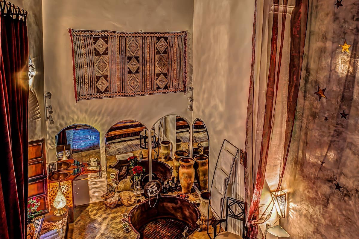 Quarto com teto de madeira, um espelho grande, cama com colcha estampada, mesa pequena com abajur e parede com tapeçaria geométrica.