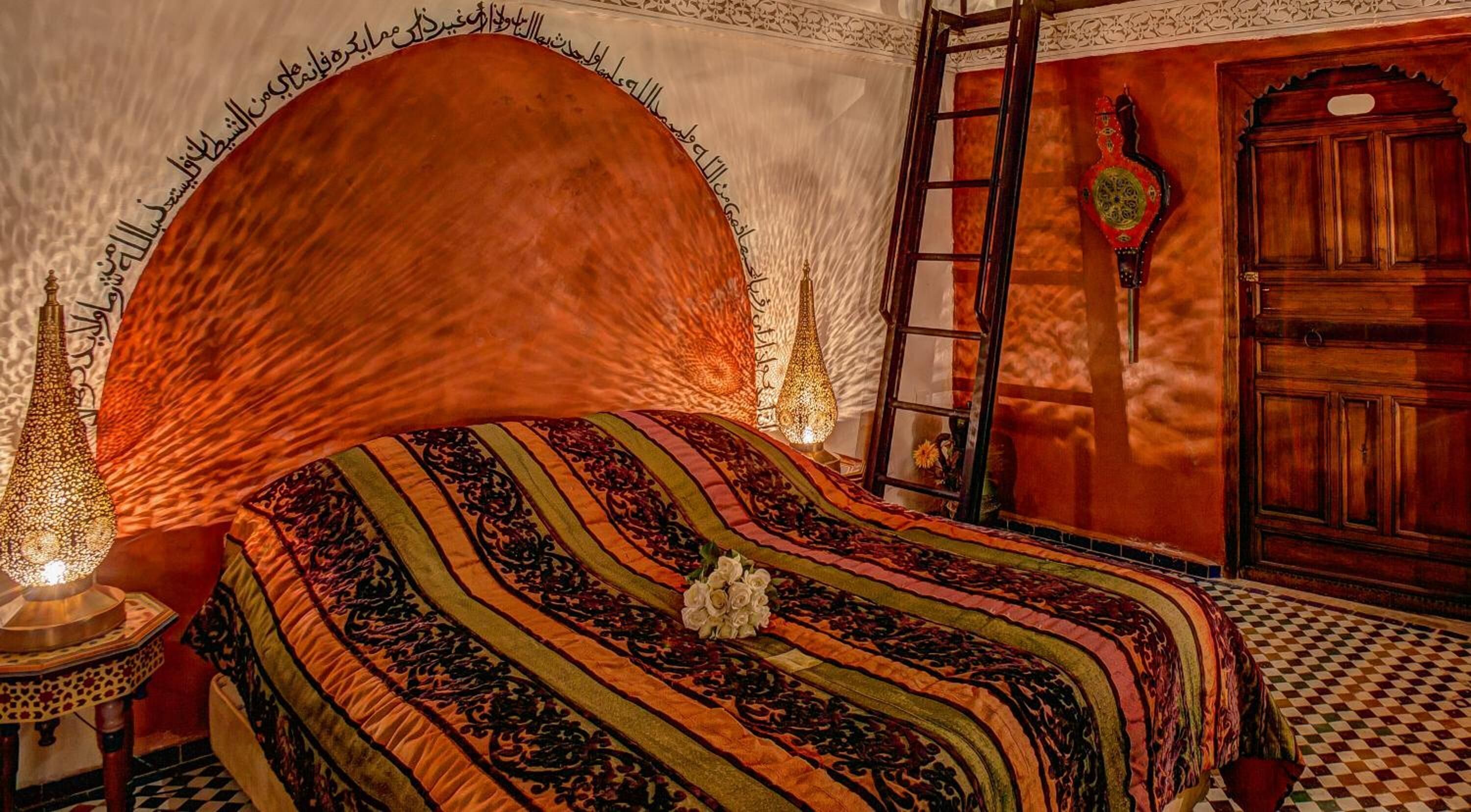 Una habitación tradicional con cama, una lámpara decorativa, una escalera y una puerta de madera.