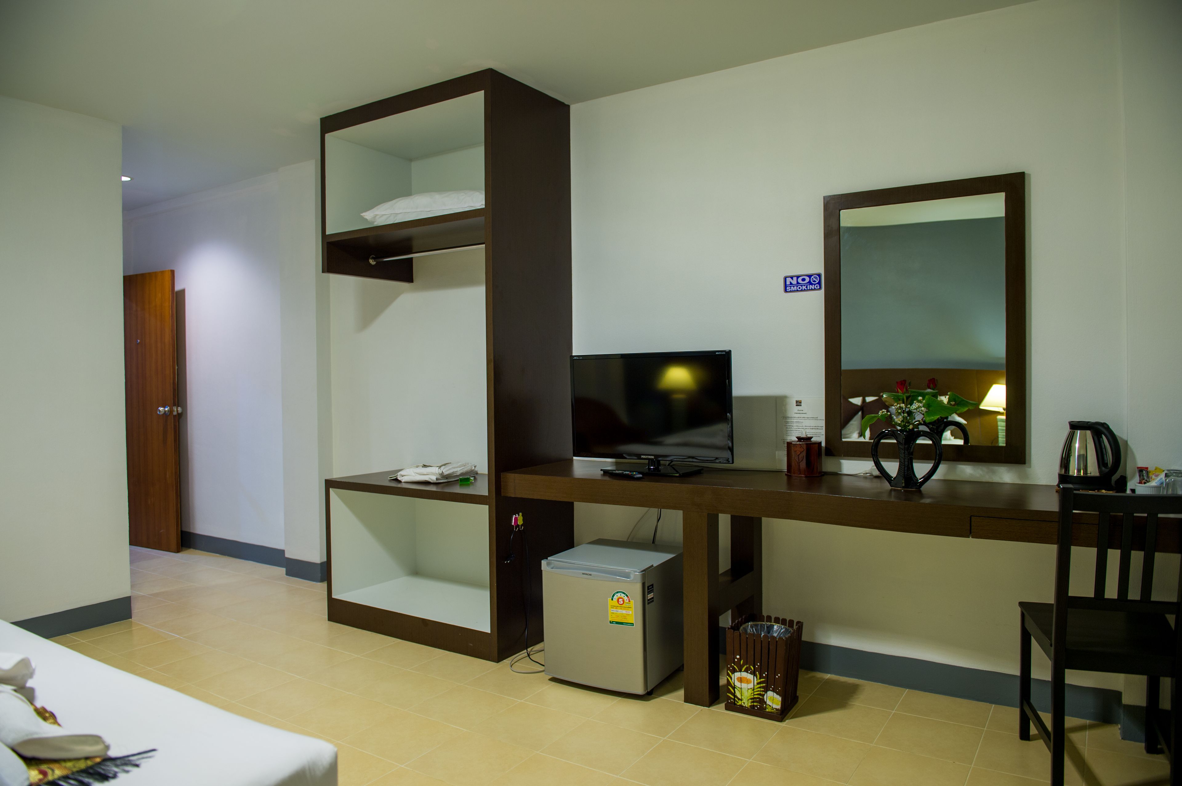 Een hotelkamer met een bed, een bureau met een computer, een kleine koelkast, een televisie en een spiegel.