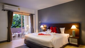 Habitación de hotel con cama, dos lámparas de noche, mesita de noche y puerta corrediza de vidrio que da a un área exterior con sillas y una mesa.