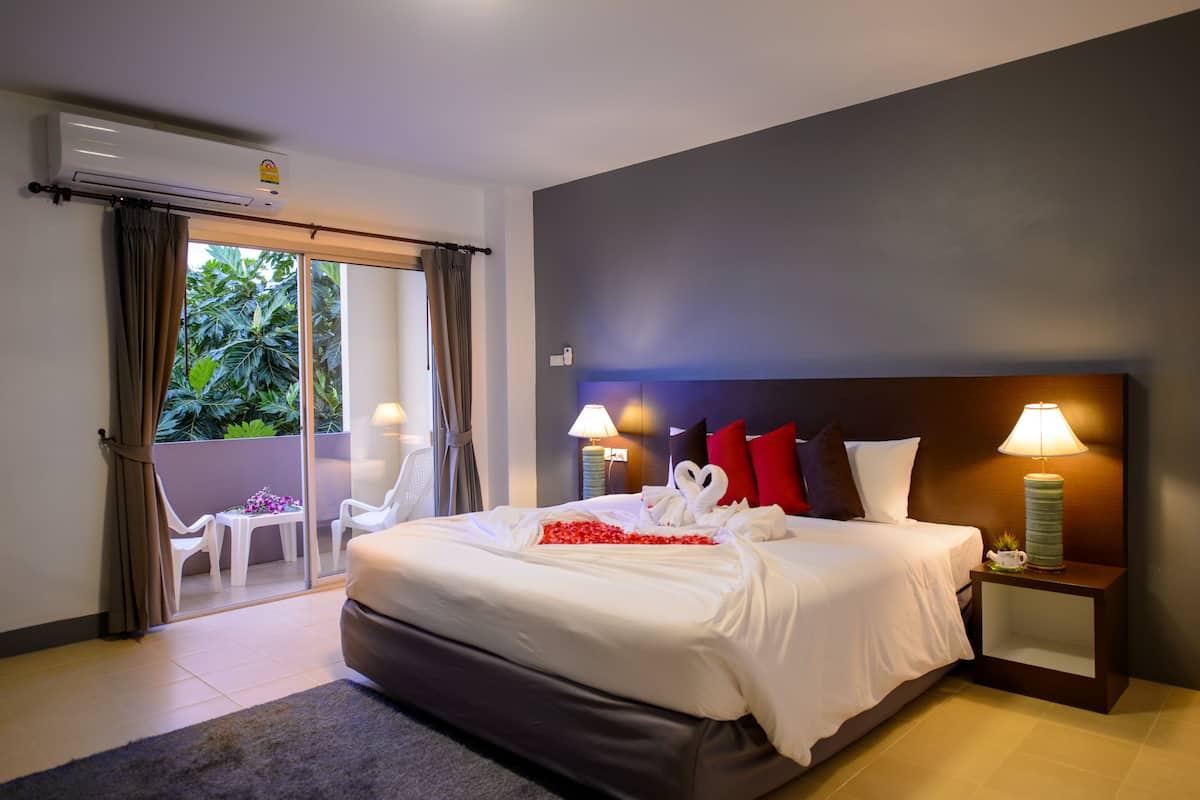 A hotel room with a bed, two bedside lamps, a nightstand, and a sliding glass door leading to an outdoor area with chairs and a table.