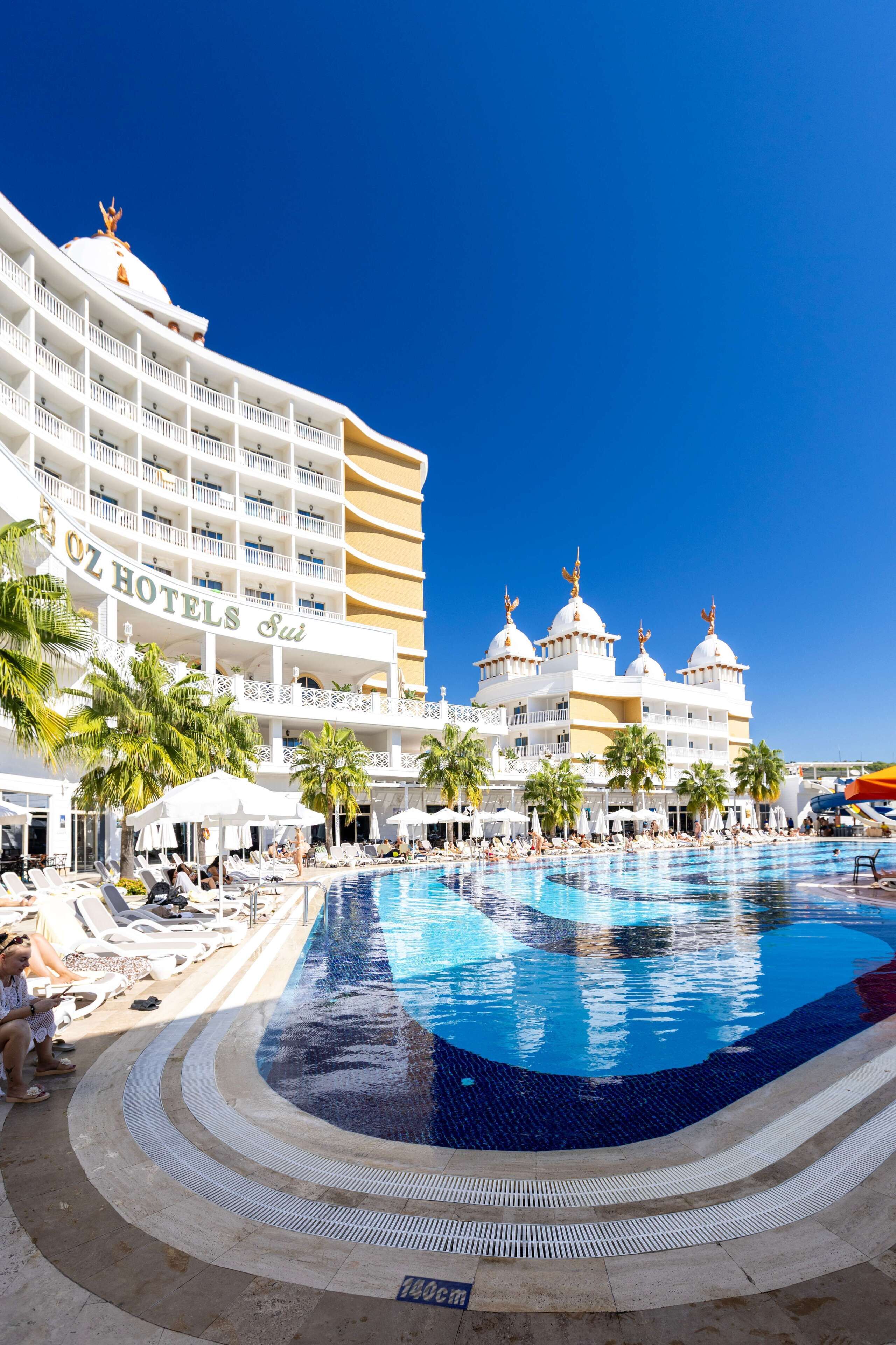 A hotel with a large pool, palm trees, and a clear blue sky.