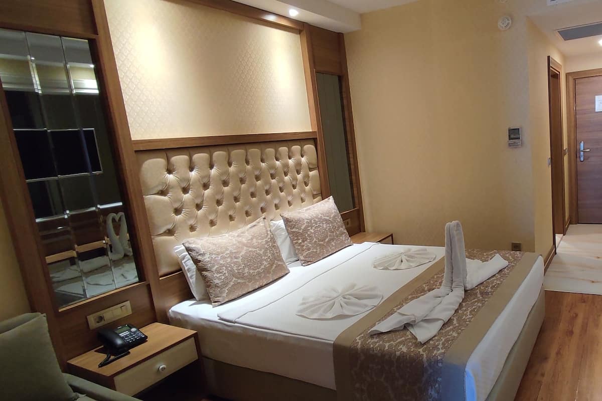 A hotel room with a large bed, a bedside table with a phone, a mirror, and a wooden floor.