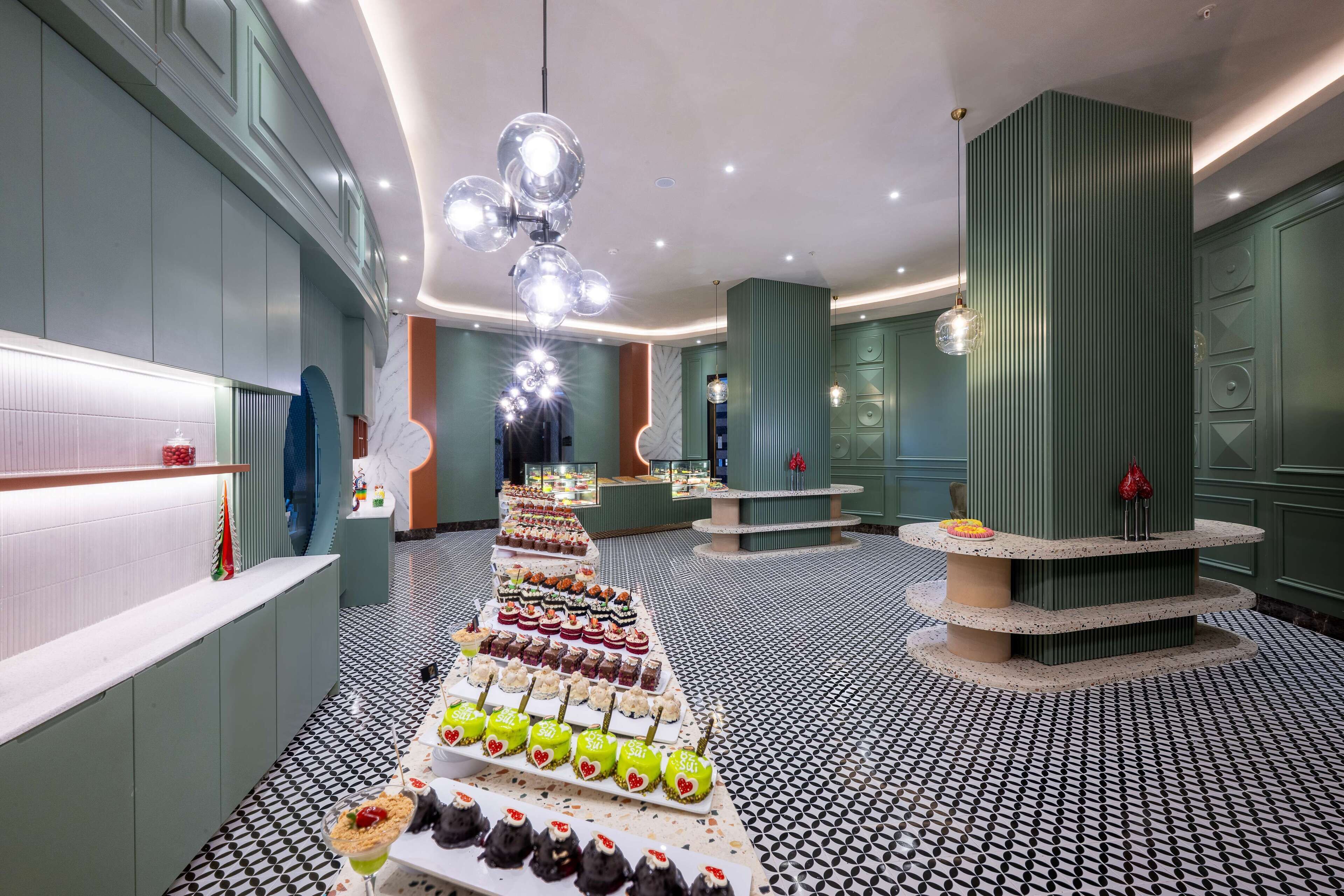 En modern hotellobby med ett centralt placerat bord för desserter, ett mönstrat golv och en unik, vertikal kolonnstruktur.