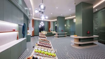 A modern hotel lobby with a central dessert display, a patterned floor, and a unique vertical column structure.