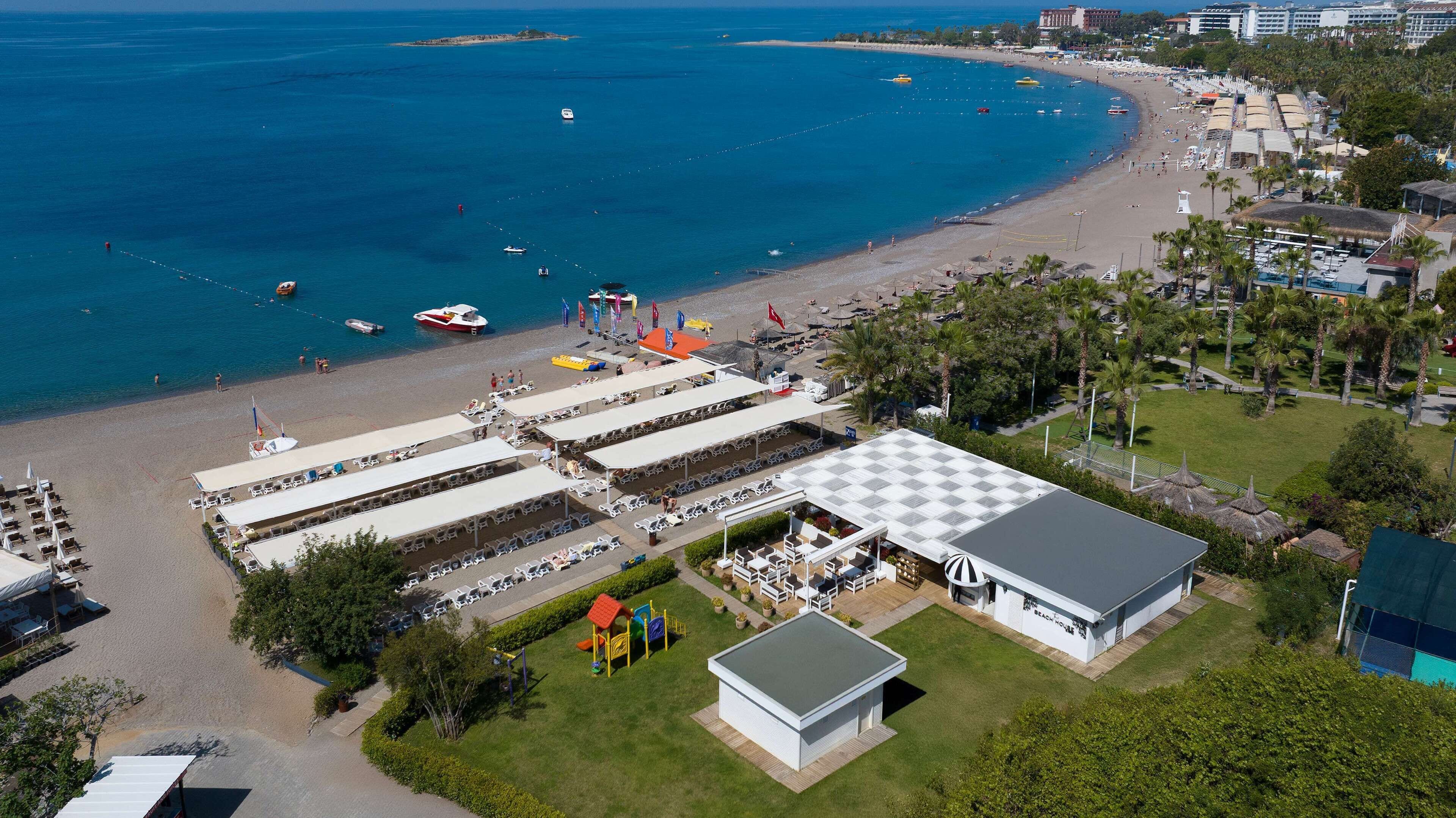 An aerial view of a beachside hotel with multiple beach umbrellas, lounge chairs, and a playground.