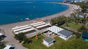 An aerial view of a beachside hotel with multiple beach umbrellas, lounge chairs, and a playground. - Oz Hotels SUI - All Inclusive (Alanya)
