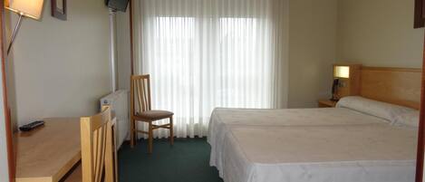 Habitación de hotel con cama, escritorio, silla, televisor y ventana con cortinas.