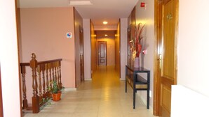 Un couloir d’hôtel avec un escalier en bois, des plantes en pot et un comptoir d’accueil.