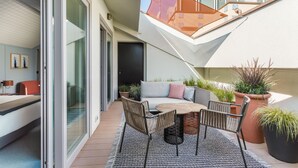 A modern outdoor living area with a sofa, chairs, and a table, surrounded by potted plants and a glass door leading to a balcony.