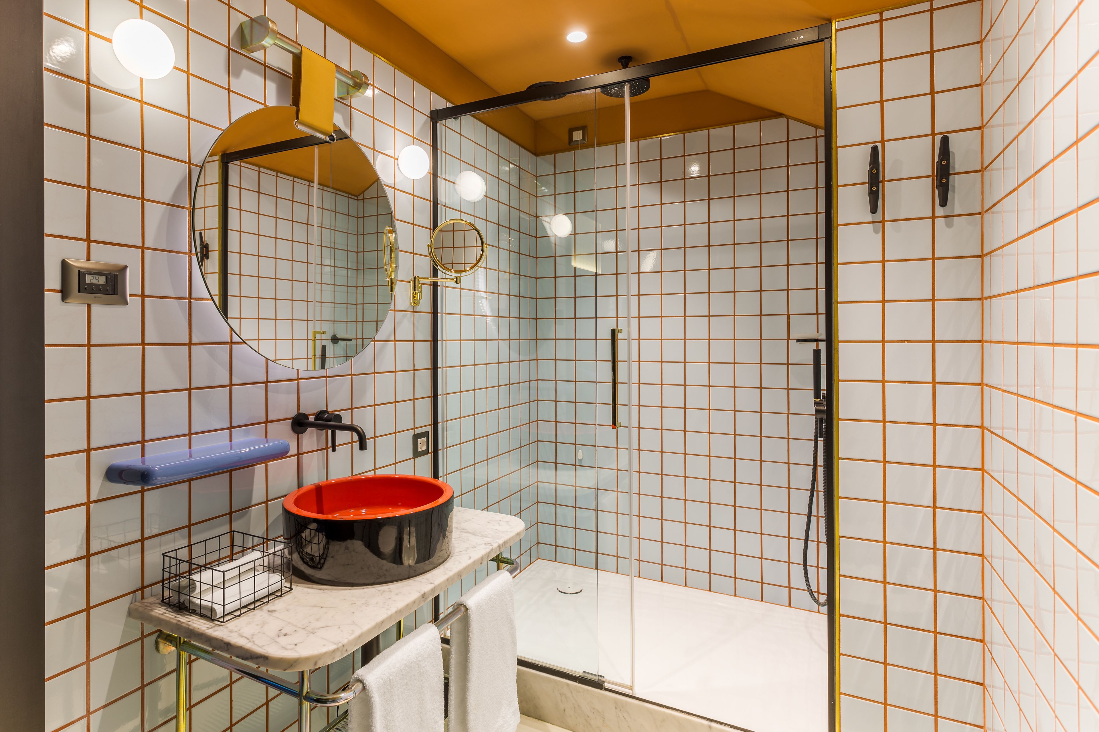 A bathroom with a glass shower enclosure, a sink with a red basin, a mirror, and a towel rack.