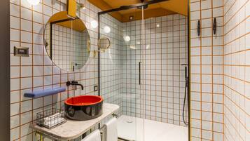 Un baño con cabina de ducha de vidrio, un lavabo con lavamanos rojo, un espejo y un perchero para toallas.