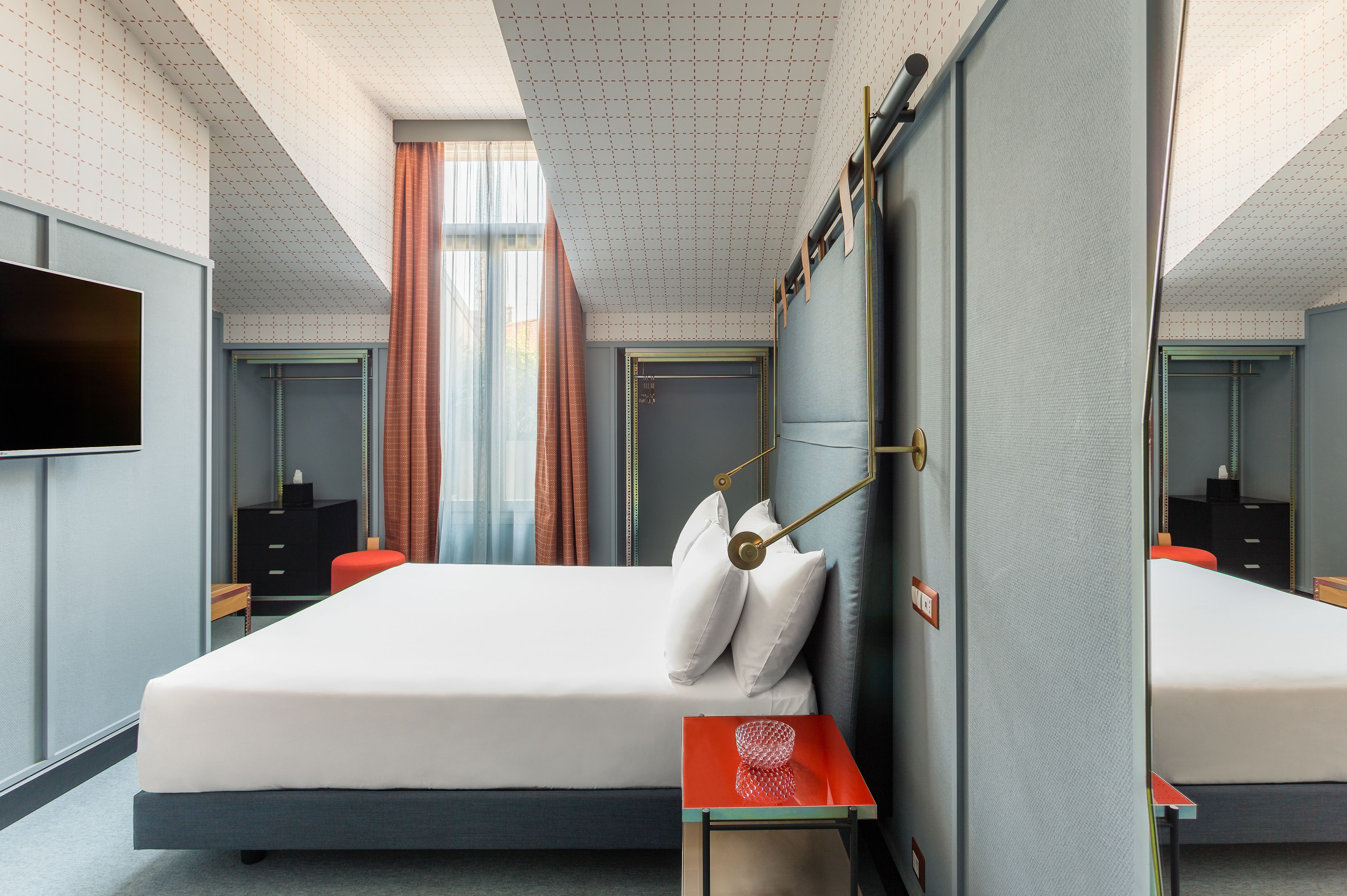 A modern hotel room with a large bed, a bedside table, a TV, and a mirror.
