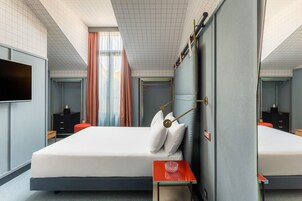 A modern hotel room with a large bed, a bedside table, a TV, and a mirror.