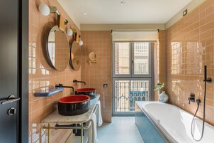 A bathroom with two sinks, a large bathtub, and a window with a view of a balcony.