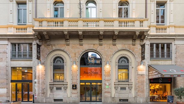 A historic building with a prominent entrance, arched windows, and a balcony with balustrades.