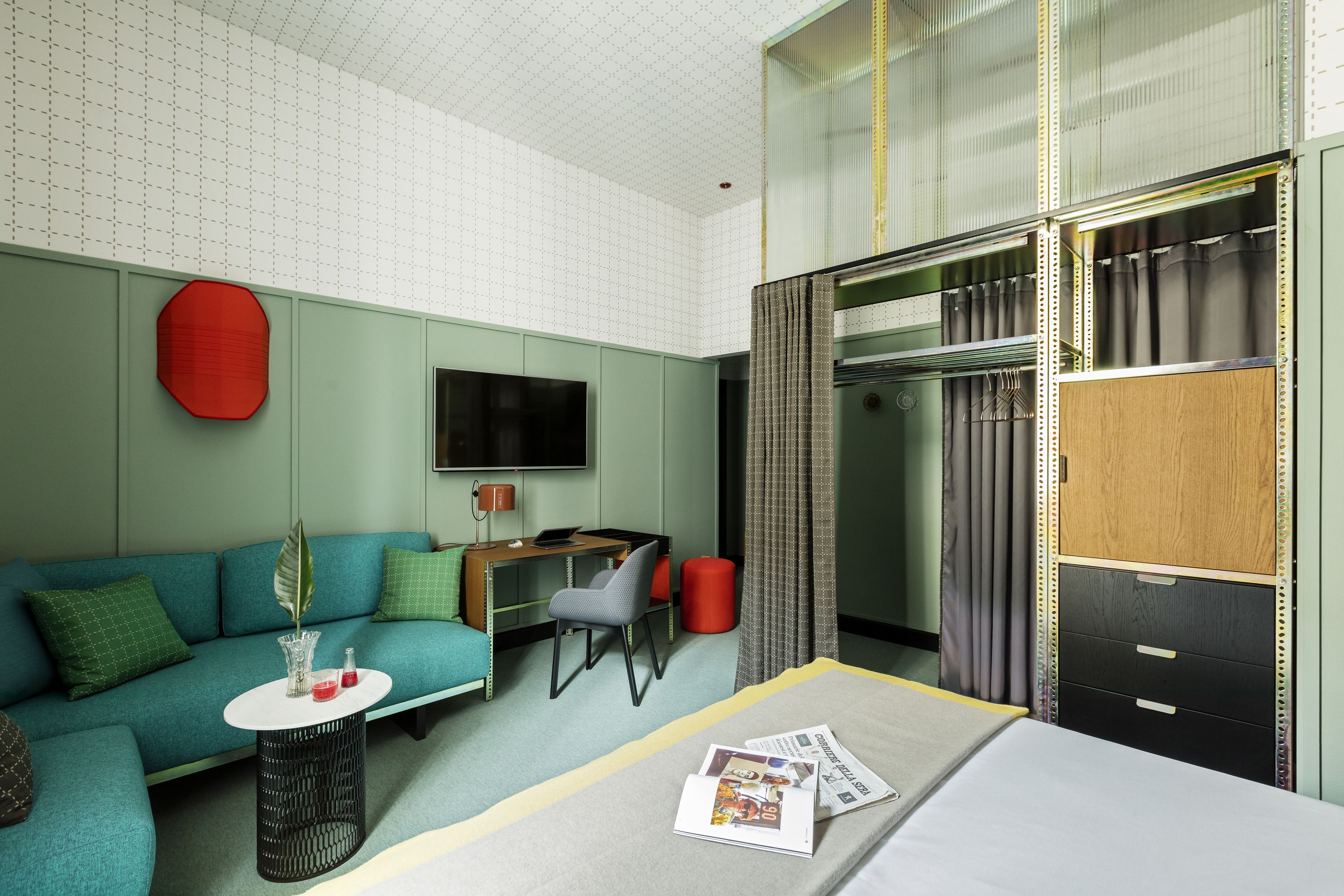 A modern hotel room with a sofa, a small table, a desk, a bed, a wardrobe, and a television.