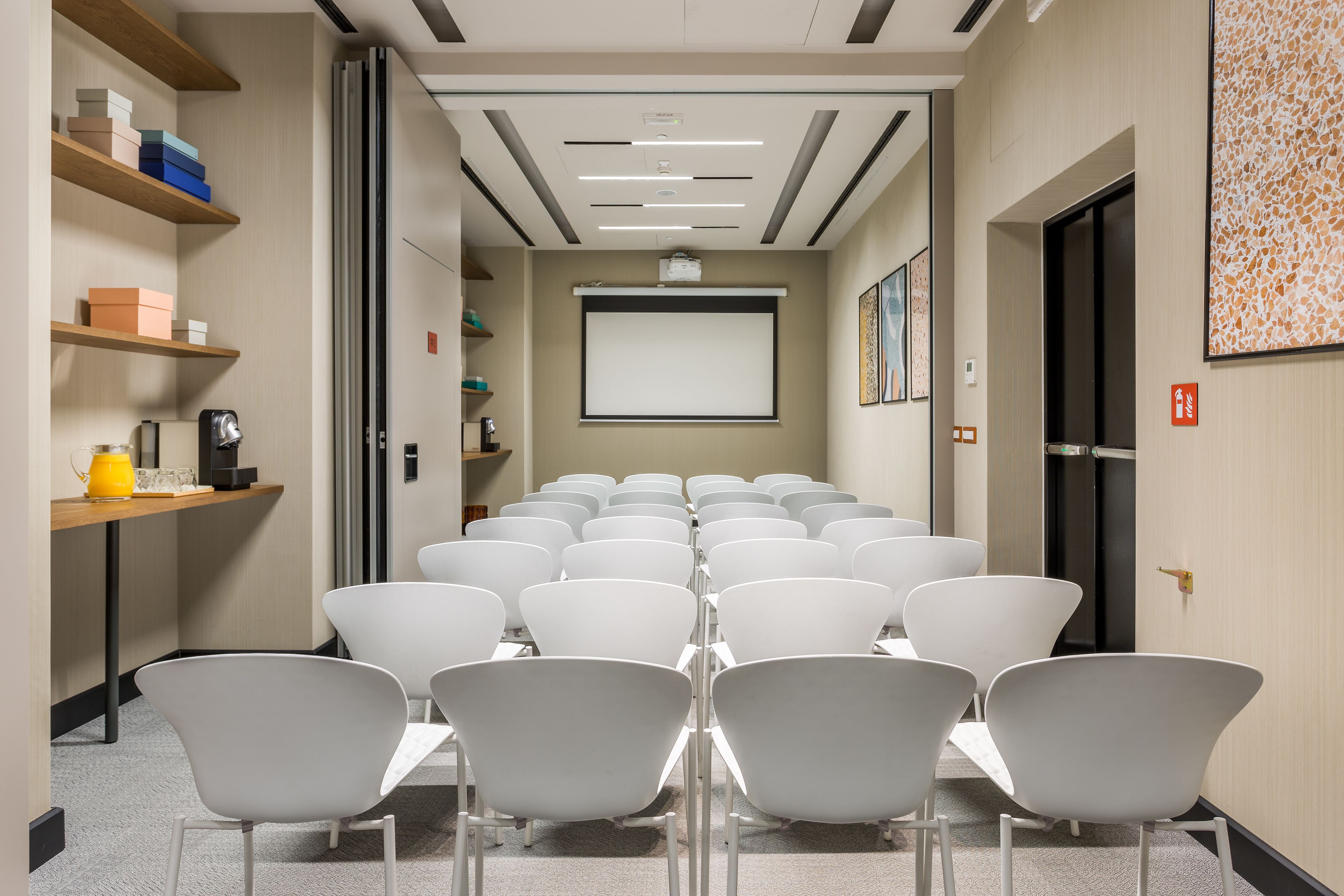 A conference room with rows of white chairs, a projector screen, and a presentation area.
