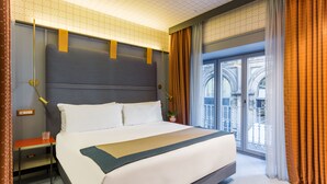 A hotel room with a large bed, a nightstand, a lamp, and a view of the outside balcony.