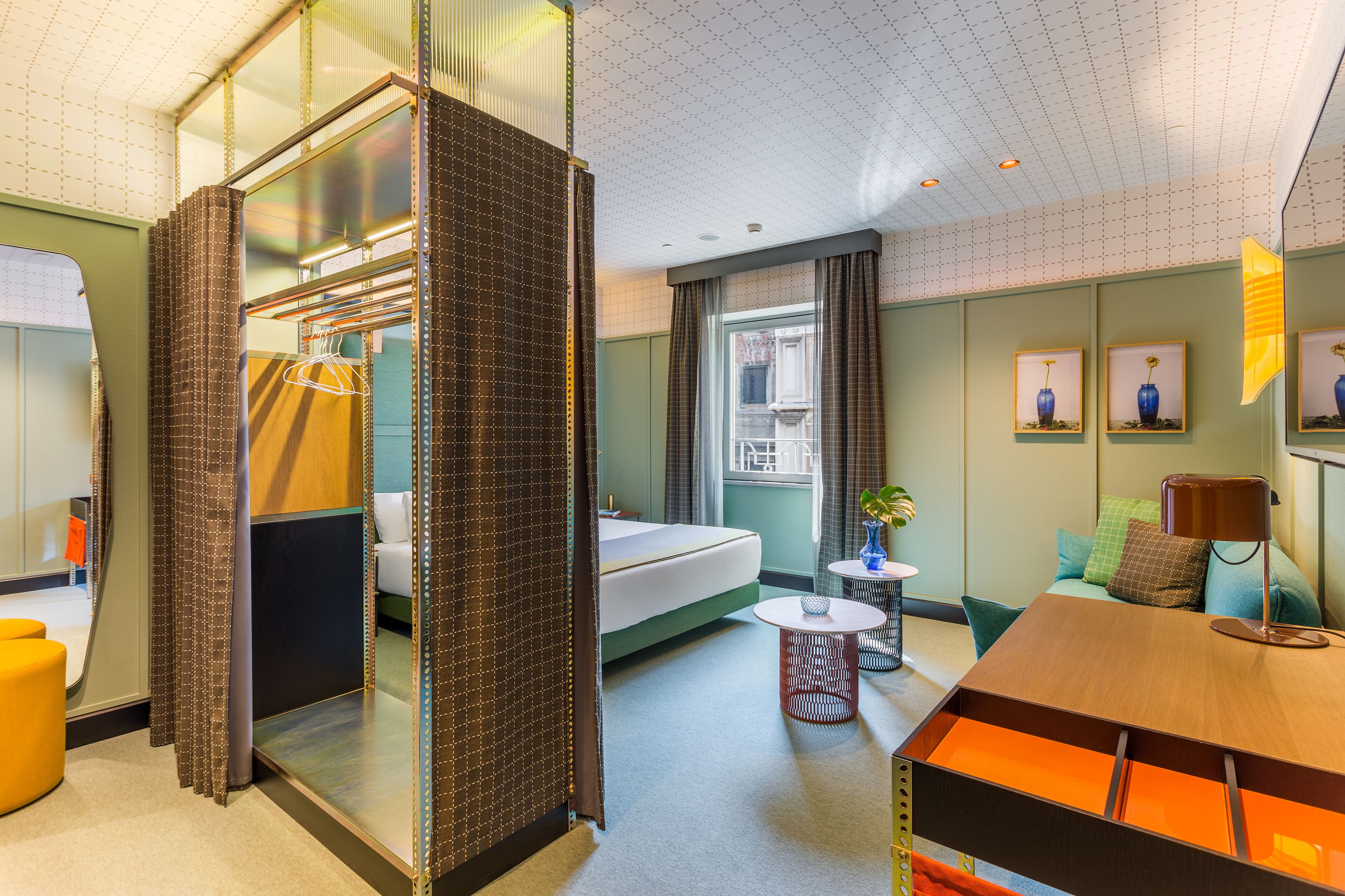 Una habitación de hotel con cama, una mesita, un espejo y una ventana con cortinas.