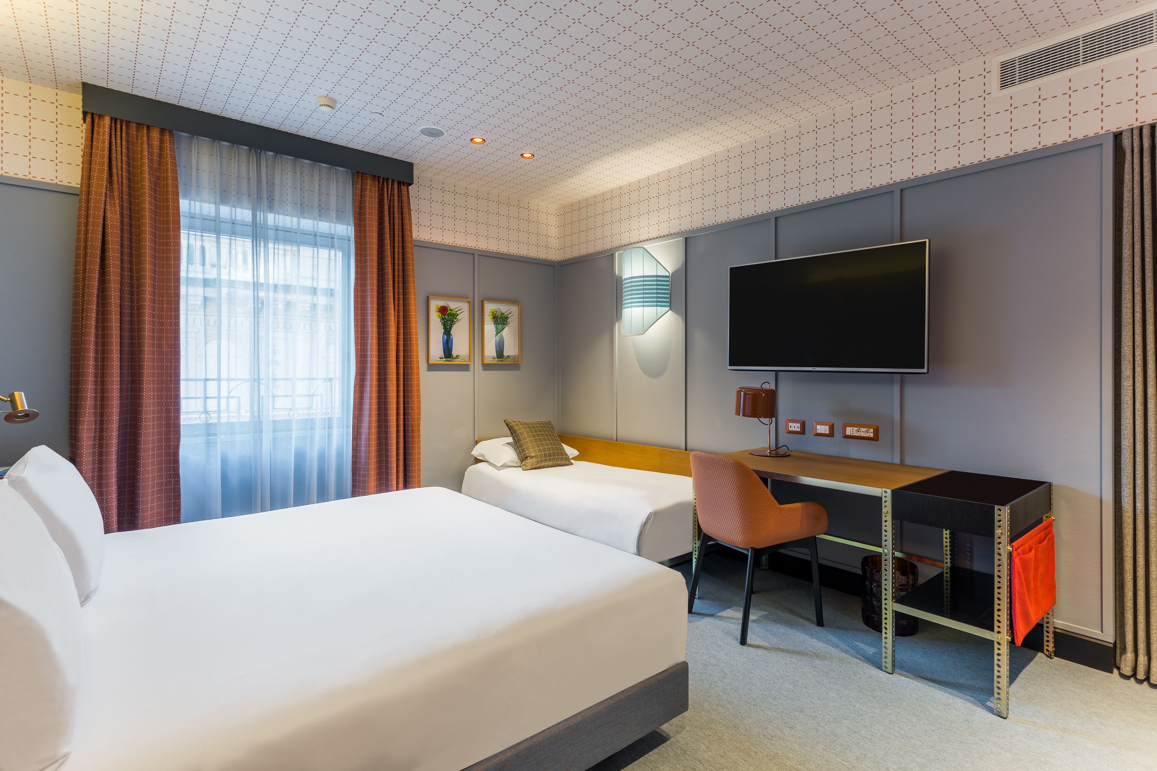 A hotel room with two beds, a desk, a TV, and a window with curtains.
