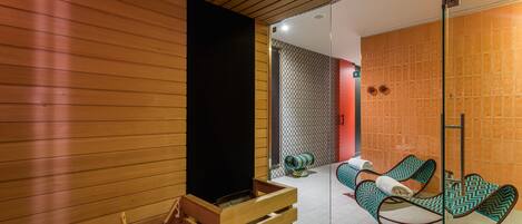 Ein modernes Badezimmer mit Holzvertäfelung, einer Glasdusche und einer Sitzecke mit gemusterten Stühlen.