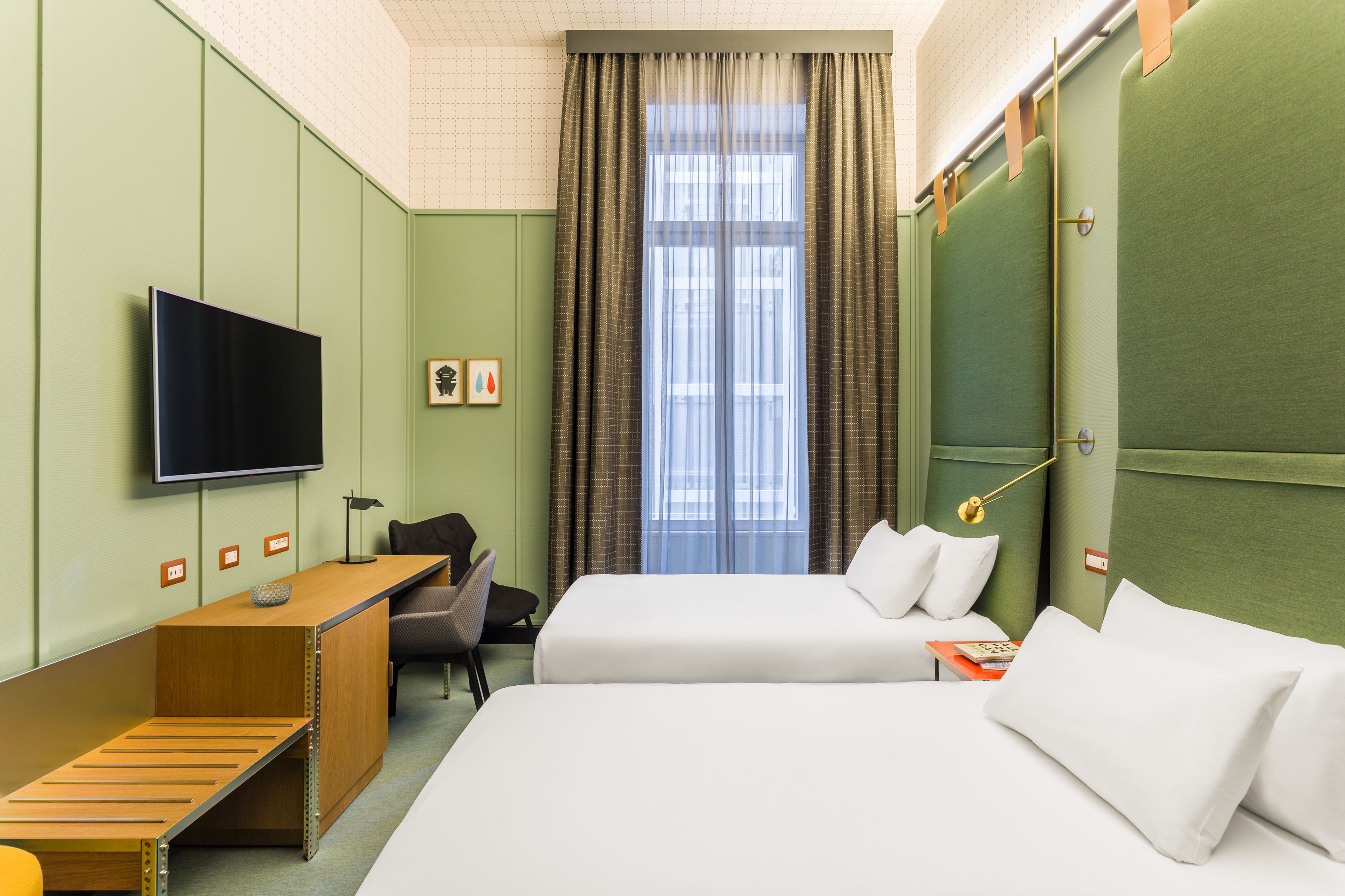 A hotel room with two beds, a desk, a chair, a TV, and a window with curtains.