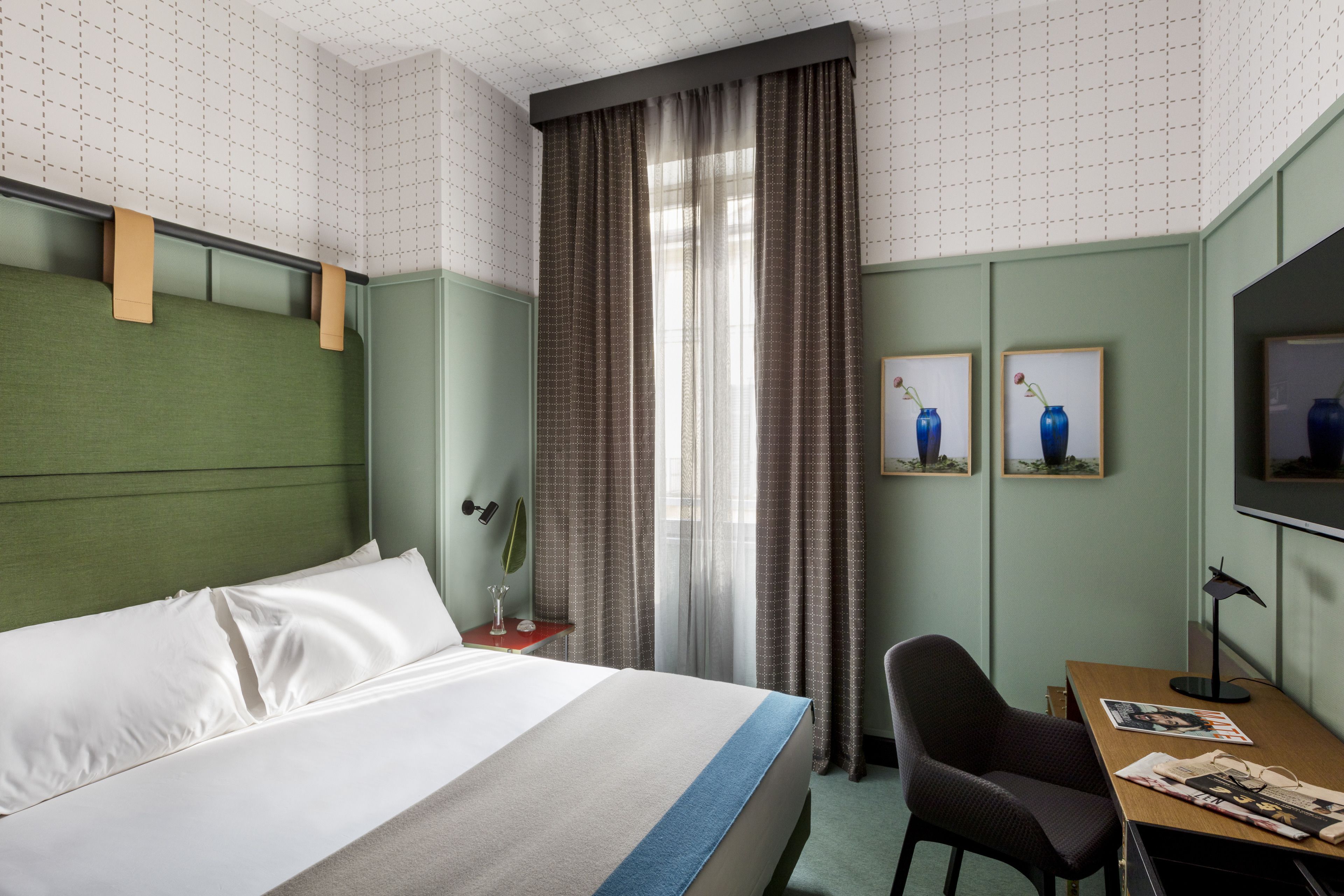Ein Hotelzimmer mit einem Bett, einem Schreibtisch, einem Sessel, einem Fernseher und zwei gerahmten Bildern an der Wand.