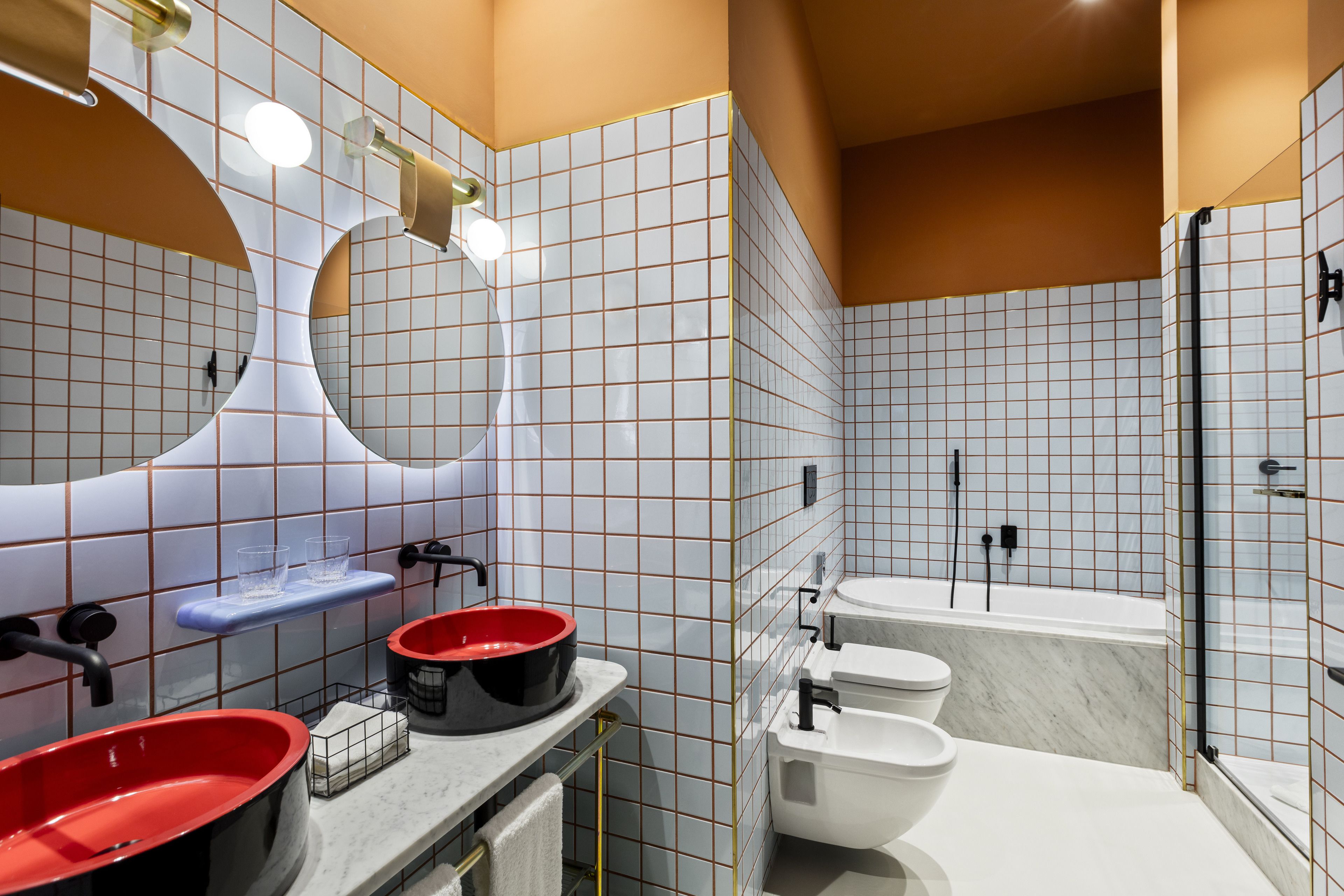 A modern bathroom with a large mirror, two sinks with red basins, a toilet, and a bathtub.