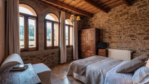 A rustic bedroom with a stone wall, a wooden bed, a nightstand, and a desk with a book. - Can Barnosell - Els Masos d'en Coll (Fontanilles)
