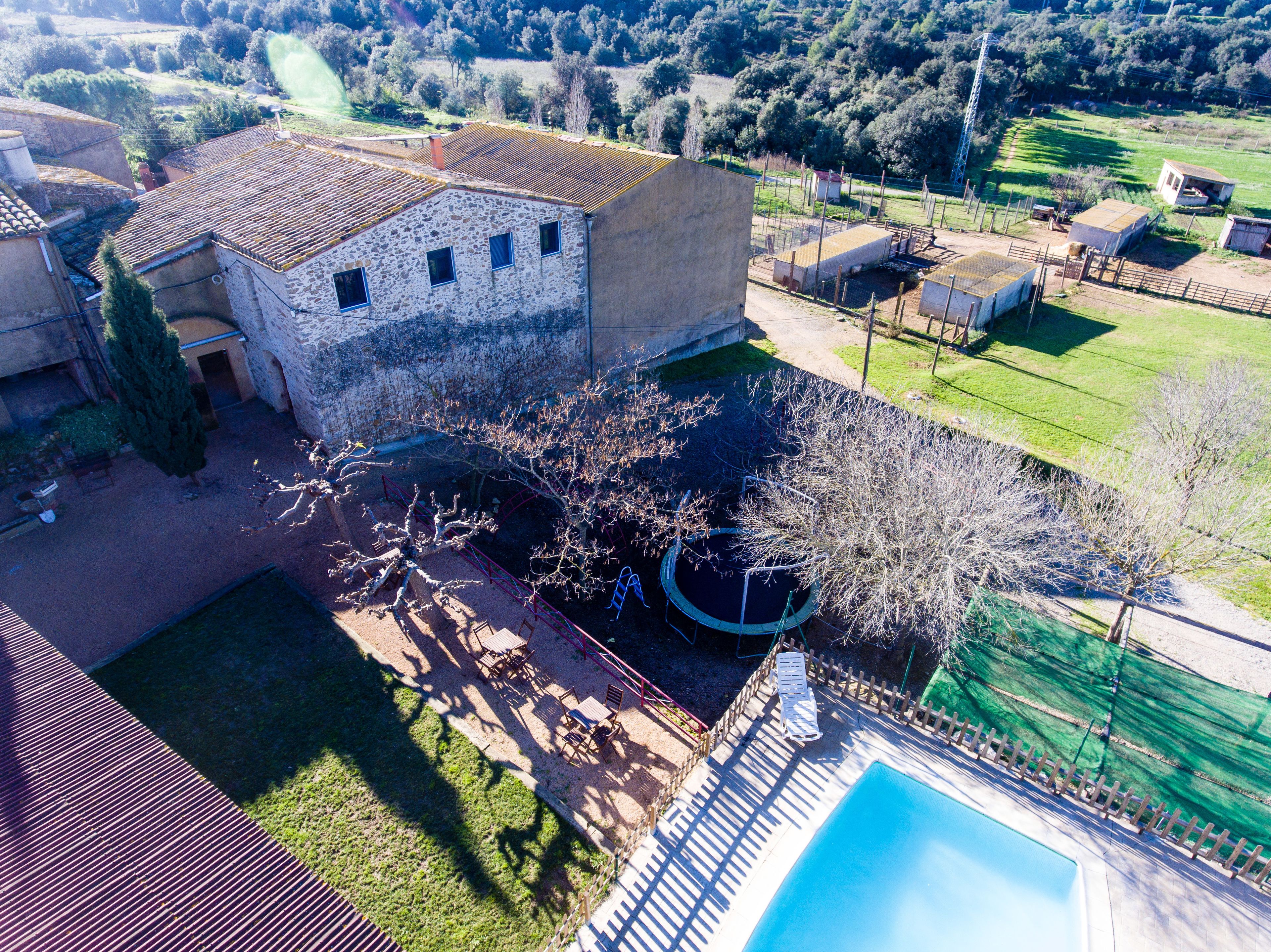 A stone building with a tiled roof, a swimming pool, and a fenced garden area.