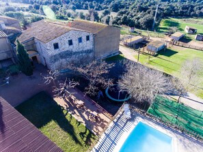 A stone building with a tiled roof, a swimming pool, and a fenced garden area.