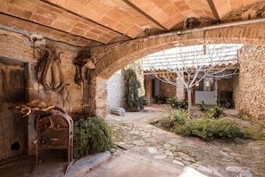 Ein altes Steinhaus mit rustikalem Inneren, mit Steinböden, Backsteinbögen und einem kleinen Gartenbereich mit Pflanzen und einem Baum.