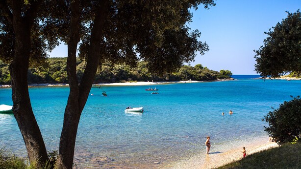 A beach with clear turquoise water, a boat, and people swimming. - Arena Indije Mobile Homes (Medulin)