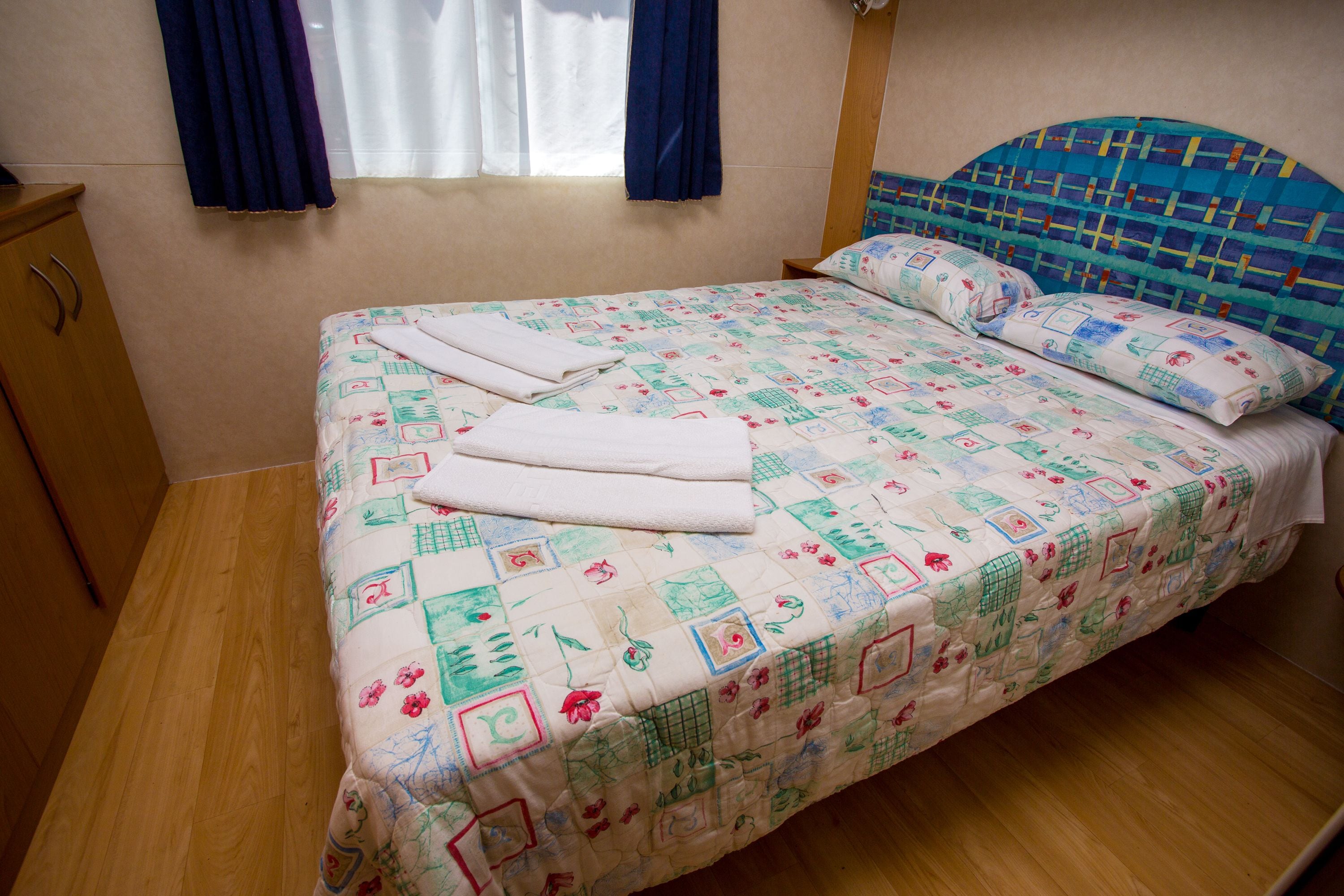 A bed with a quilted headboard, a wooden wardrobe, and a window with curtains.