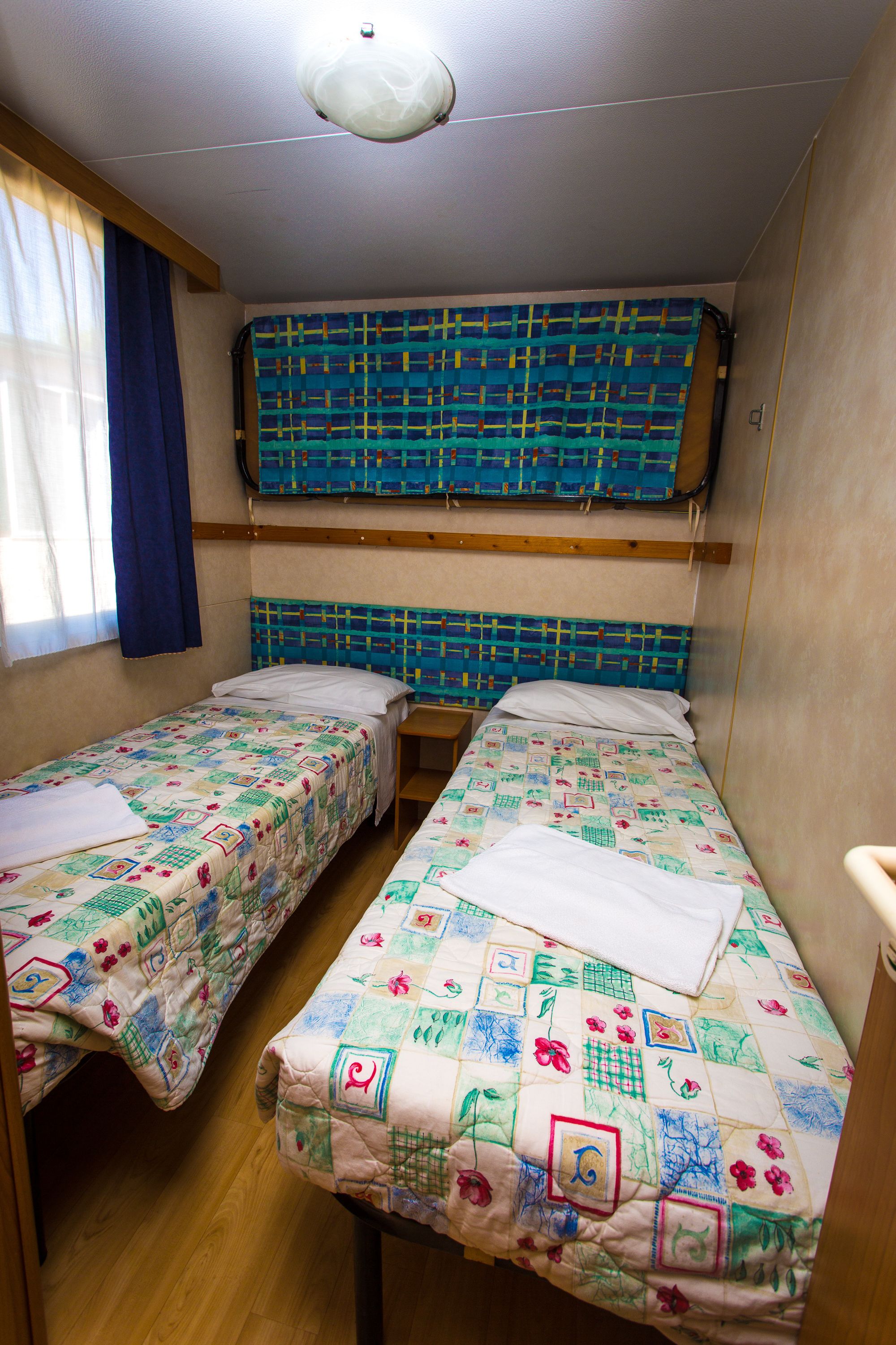 Una camera nel dormitorio con due letti singoli, pavimento in legno, un letto a castello sopra e una finestra con tende.