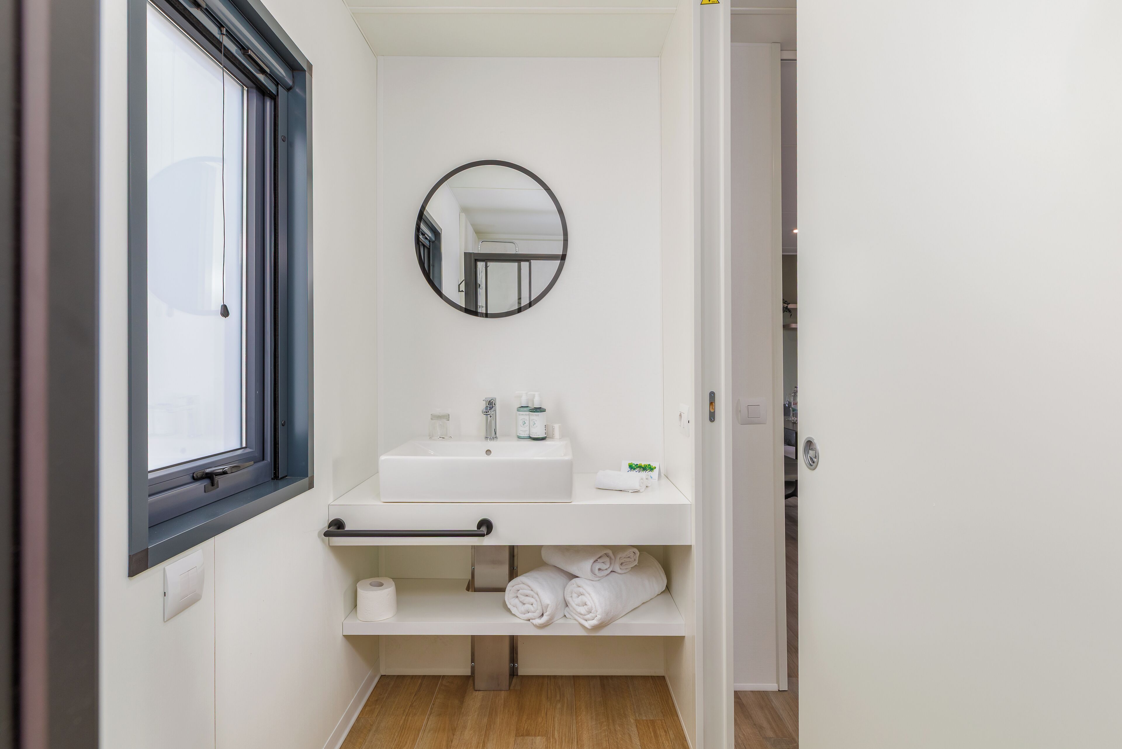 A compact bathroom with a window, a sink, a mirror, and a towel rack.
