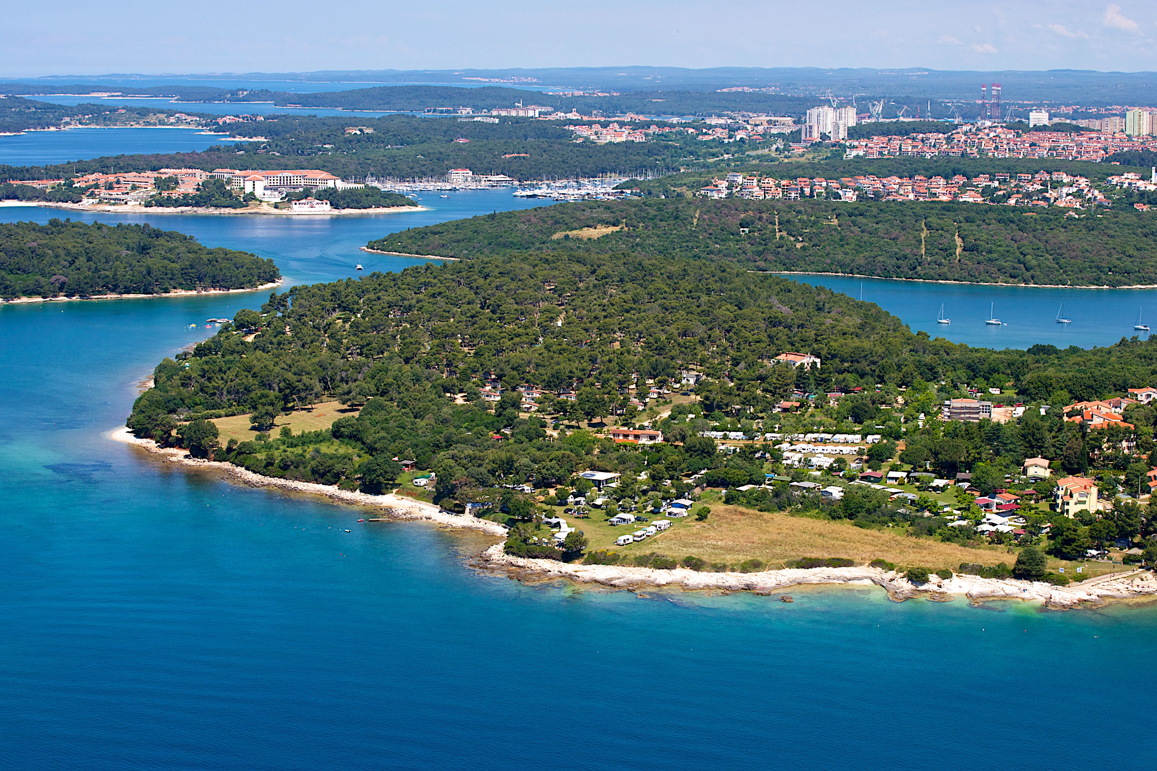 Una vista aerea di una località costiera con un porto turistico, vegetazione lussureggiante e zone residenziali.