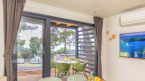 A room with a table set for dining, a TV on the wall, and a view of the outdoors. - Arena Indije Mobile Homes (Medulin)